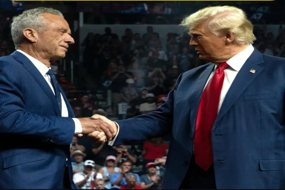 Robert F. Kennedy Jr. and Donald Trump shaking hands at a public event, both wearing blue suits, in front of a cheering crowd.