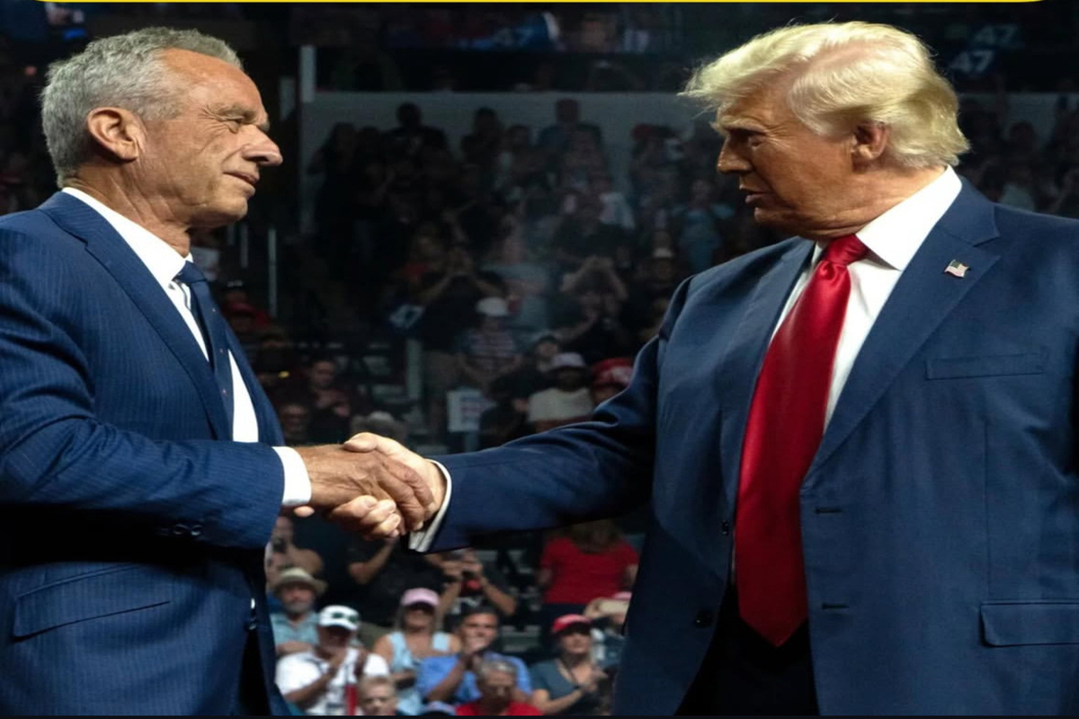 Robert F. Kennedy Jr. and Donald Trump shaking hands at a public event, both wearing blue suits, in front of a cheering crowd.