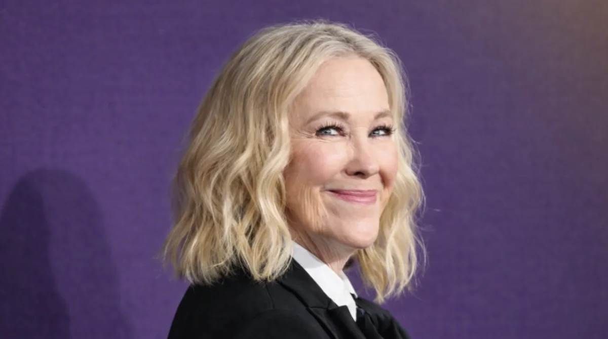 Elegant middle-aged woman smiling at a red carpet event with a soft purple background