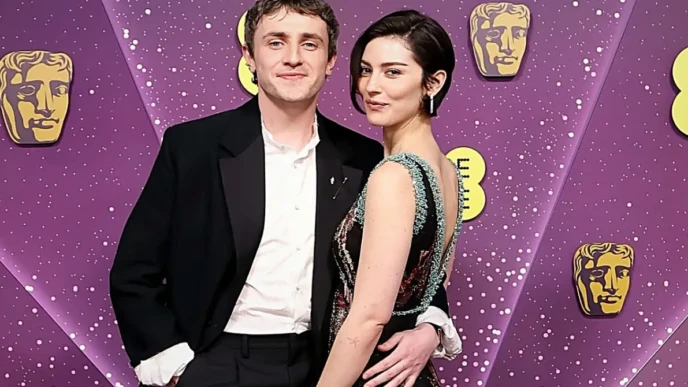 Gracie Abrams posing on the BAFTA Awards red carpet with a guest, against a purple BAFTA backdrop.