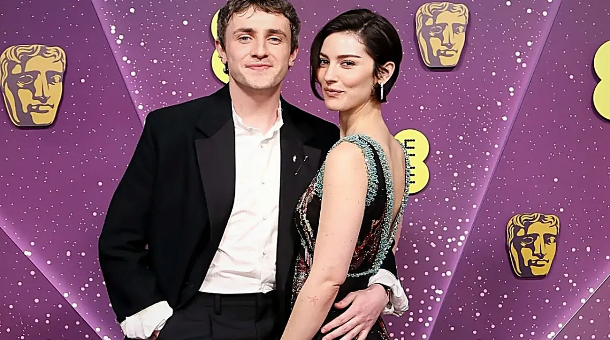 Gracie Abrams posing on the BAFTA Awards red carpet with a guest, against a purple BAFTA backdrop.