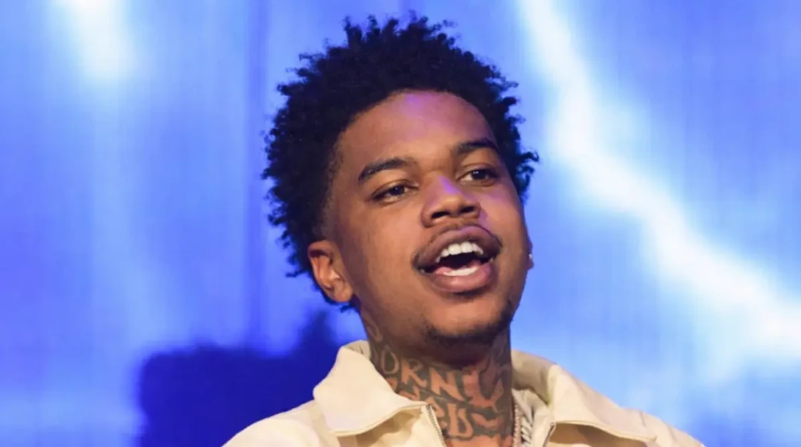 Lil Poppa performing live on stage in an off-white jacket under blue lighting