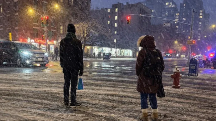 new york city ban scene at a snowy night intersection with pedestrians waiting to cross and traffic lights glowing