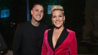 Pink smiling at an evening event wearing a hot pink velvet blazer, posing with her husband in a black suit.