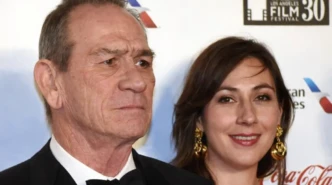 Tommy Lee Jones posing at a red carpet event with a woman in the background.