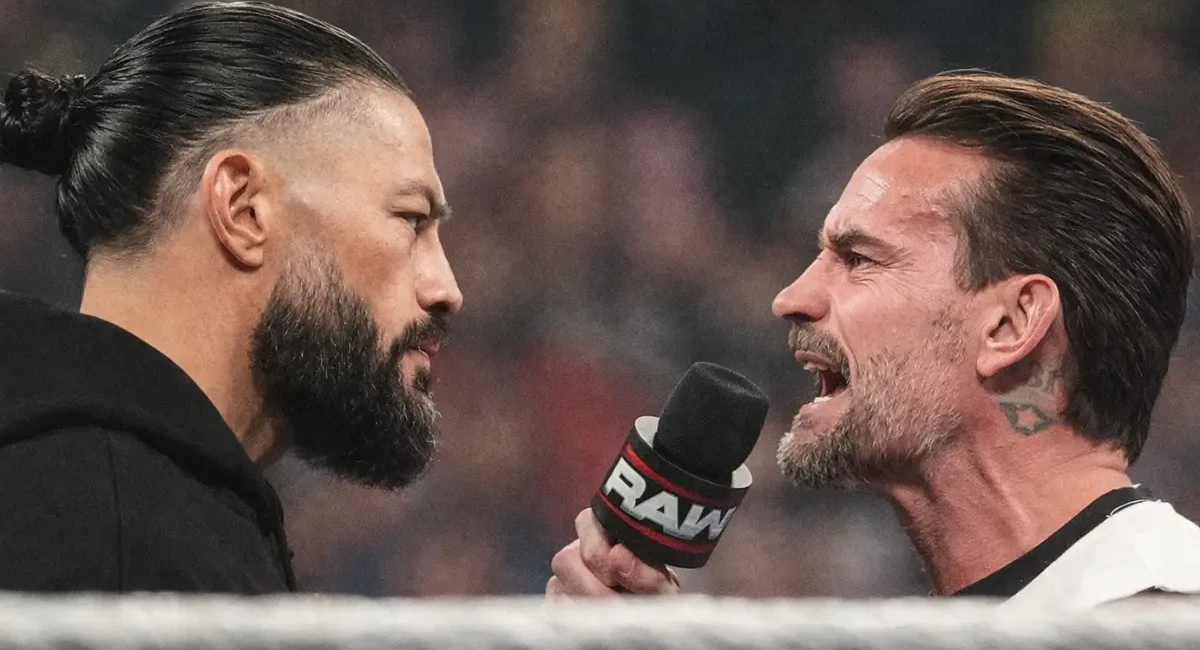 Roman Reigns stares down CM Punk during a heated RAW in-ring confrontation as Punk shouts into a microphone.