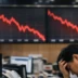 South Korean stock exchange trading floor with falling red market charts on large screens as a trader reacts to the sharp market decline